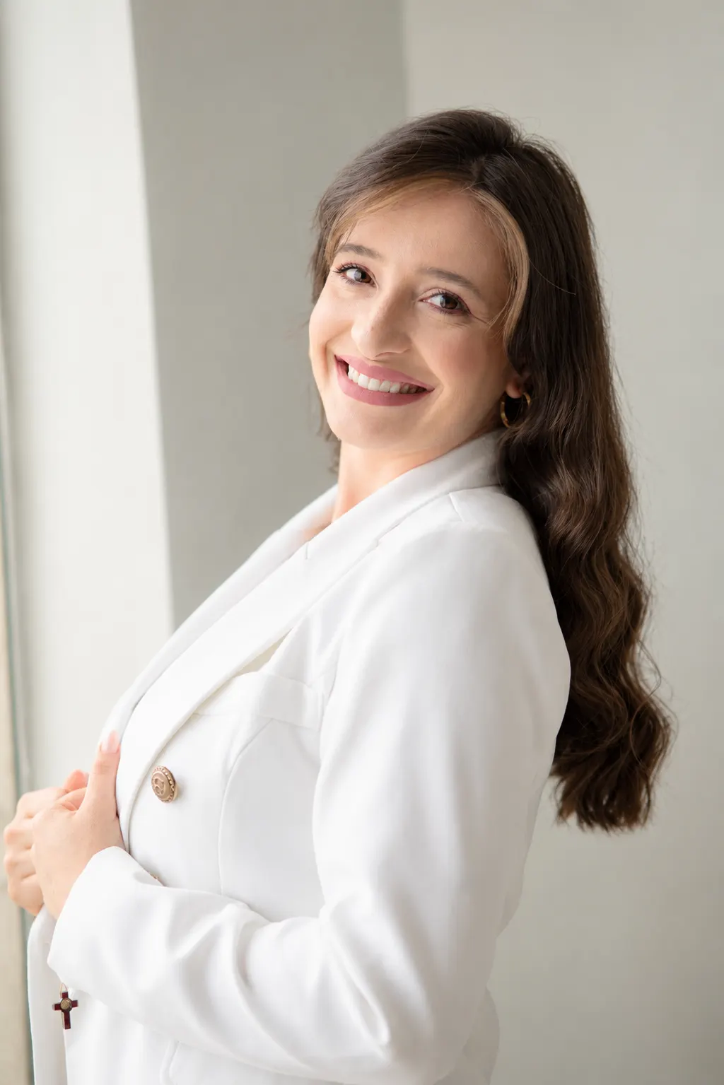 Thaissa Vargas sorrindo, de blazer branco, perto da janela
